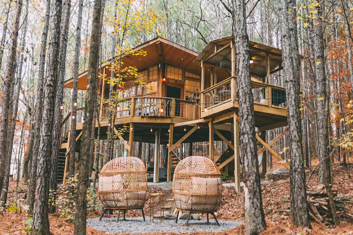 View of two adorable nested chairs facing the treehouse in an autumn forest. This treehouse is one of the best airbnbs in Alabama. 