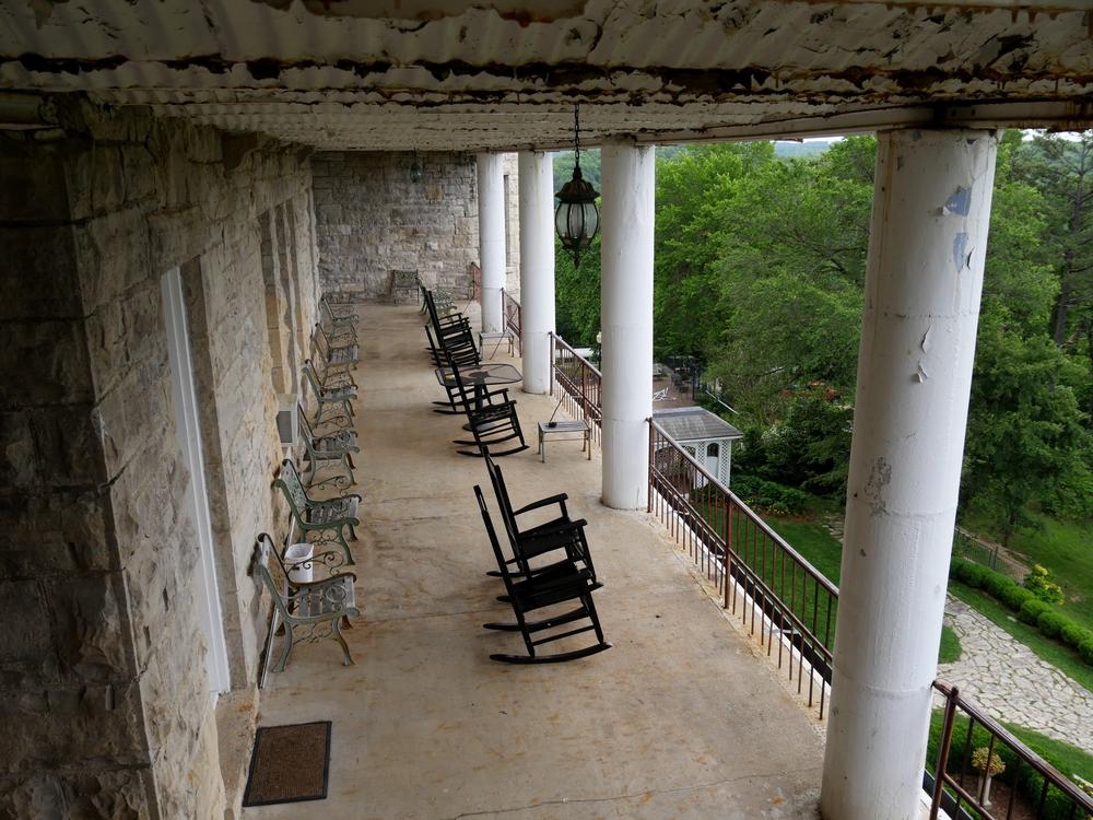 the porch of Crescent Hotel & Spa with black rocking chairs and white detailing looking out over green trees