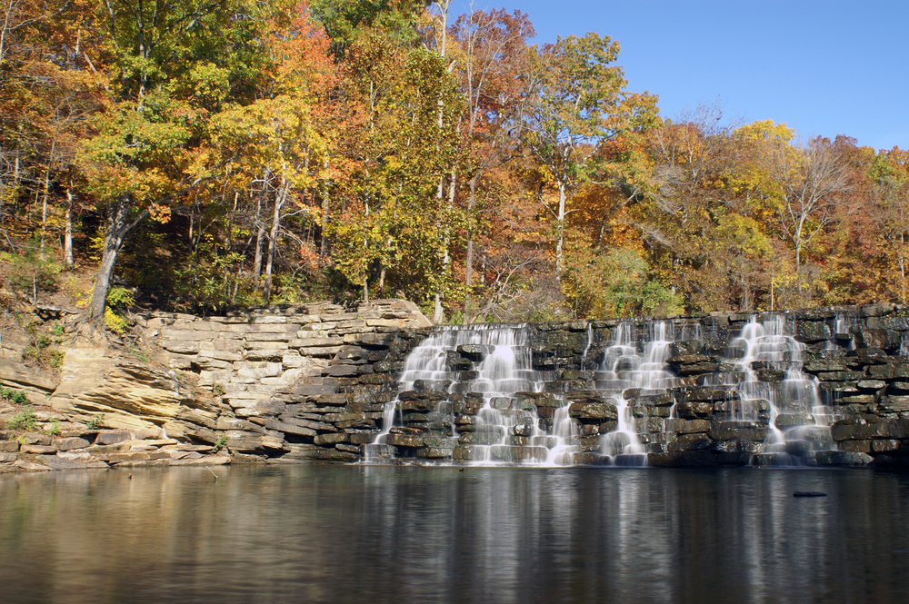 Devil's Den State Park with a waterfall and fall foliage trees in orange and yellow color with blue sky