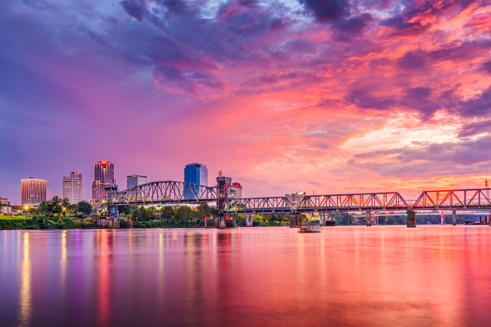 pink sunset on the water over Little Rock with buildings and a bridge in the distance that is one of the best things to do in Arkansas. 