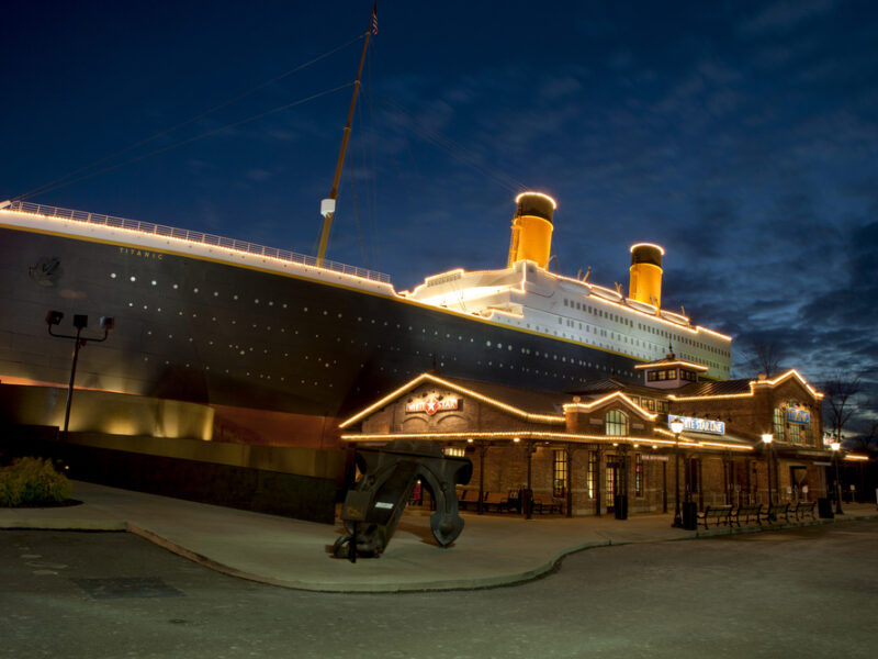 A nighttime view of the Titanice Museum, shaped like the boat itself, huge and lit up across the decks. 