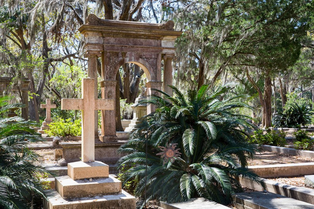 Mossy trees and palms stand over large graves at Bonaventure Cemetery, where one of things to do in Savannah is to take a tour of the cemetery. 