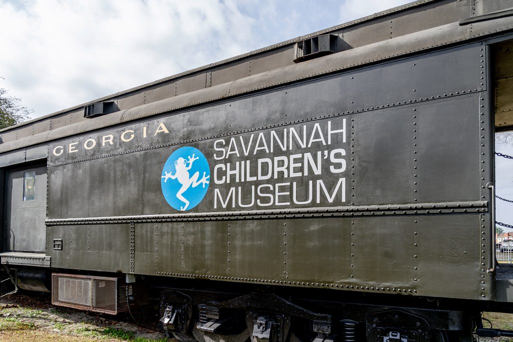 The logo of Savannah Children's Museum, which includes a frog, painted onto an old railcar. Visiting the museum is one of the best things to do in Savannah with kids.