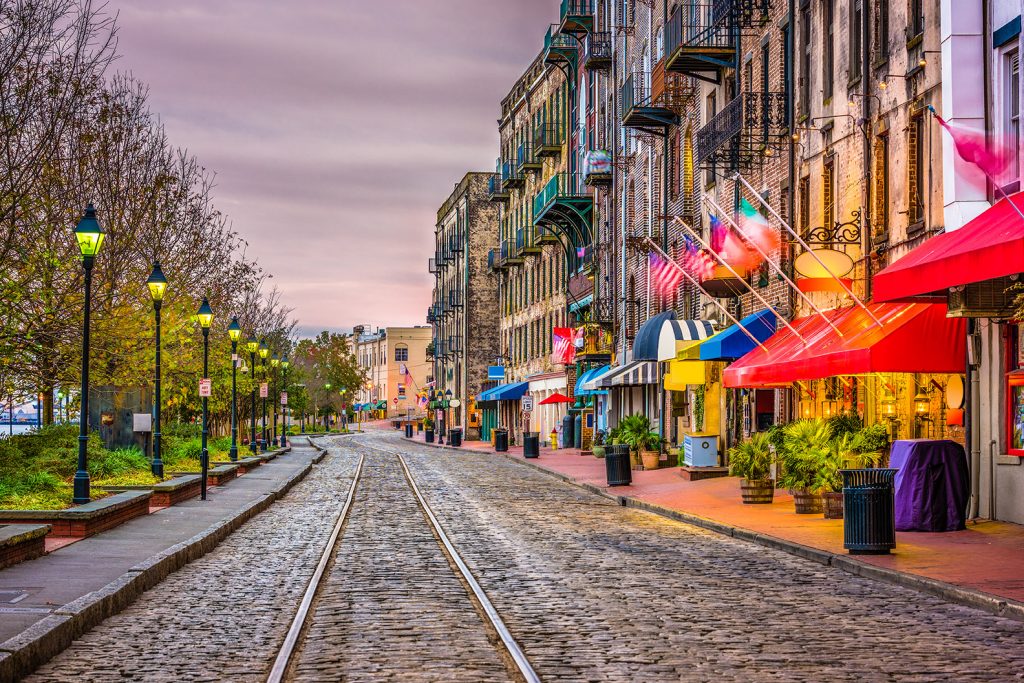 Trolly tracks on cobbled streets, with streetlamps and colored awnings along River Street in Savannah.