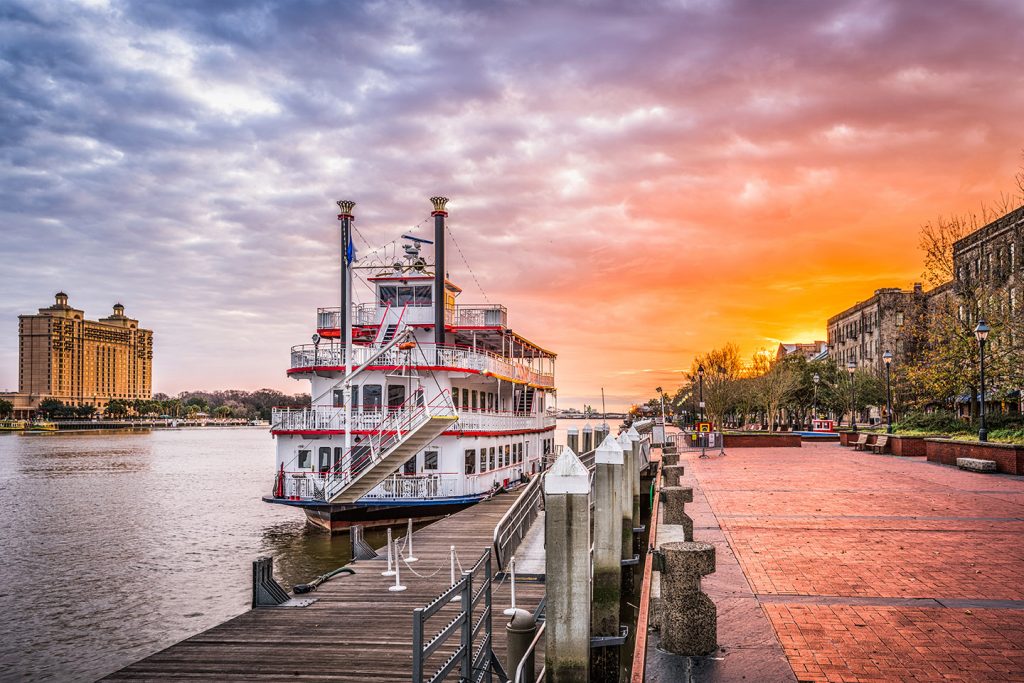 A three-tiered white riverboat sits along a dock at sunset in Savannah. A river cruise is one of the best things to do in Savannah.