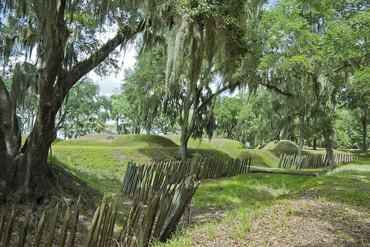 Moss-covered trees stand over grassy earthen mounds at Fort McAllister in Richmond Hills, Georgia.