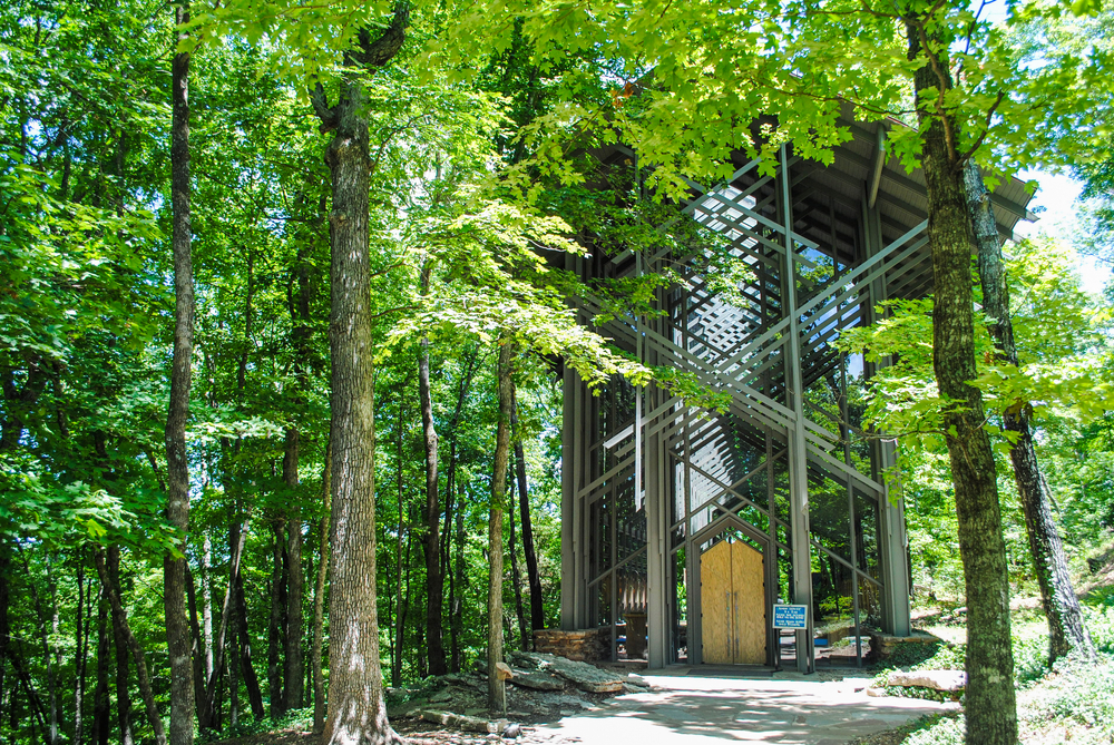 Thorncrown Chapel is a popular tourist destination in Arkansas.it is a brown chapel with a wooden door with green leaves everywhere