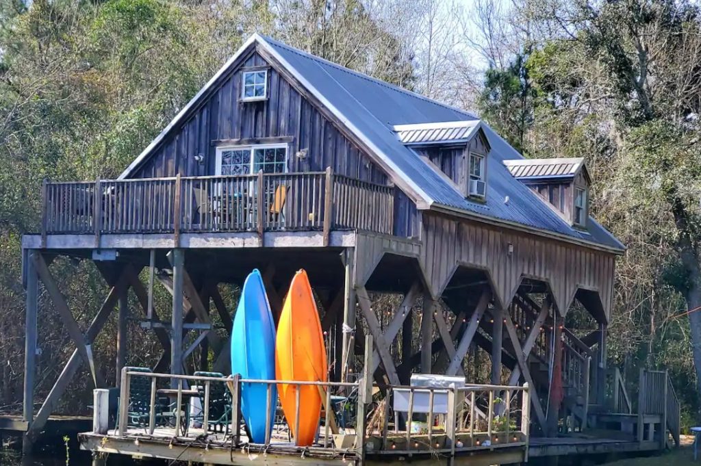 A cabin on stilts that overlooks the Louisiana Bayou that has its own dock with a grill, chairs, and kayaks