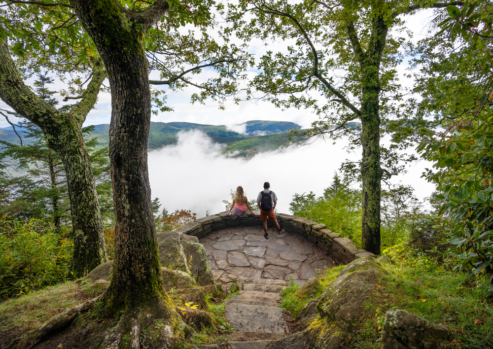 A couple standing in a stone overlook in the Blue Ridge Mountains while clouds roll through the mountains