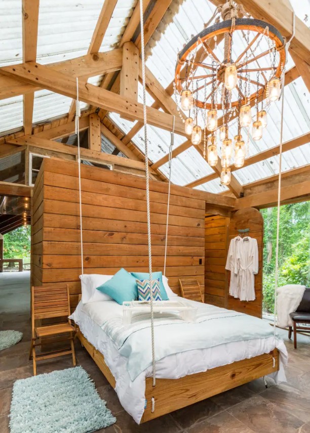 A suspended bed with a chandelier above it in a cabin full of windows in Texas