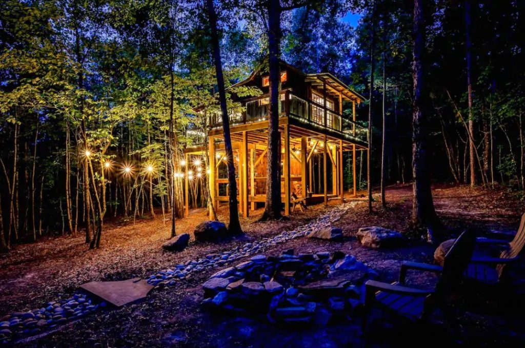 A cabin in the woods during twilight lit up by string lights in South Carolina one of the coziest cabins in the south