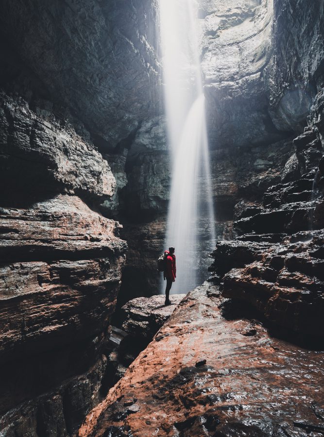 A person standing next to a waterfall flowing down one of the best caves in Alabama Stephens Gap