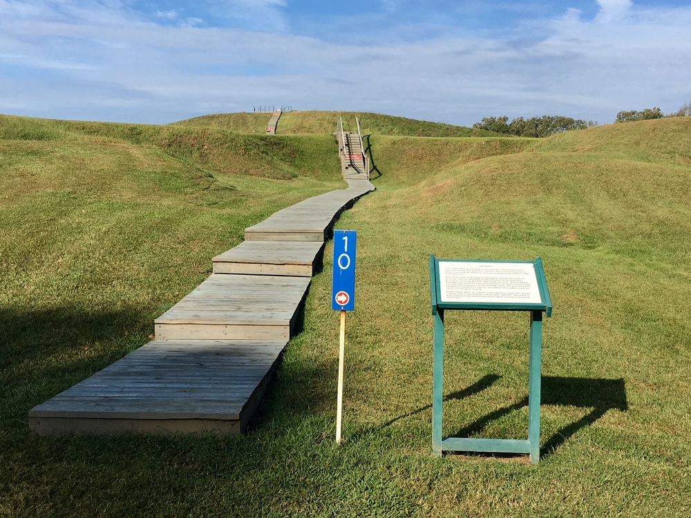 Photo of a boardwalk trail with steps leading up an earth mound at Poverty Point World Heritage Site, one of the most interesting places to hike in Louisiana.