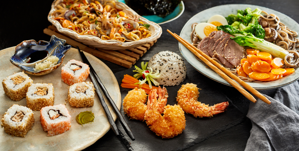 Photo of a spread of sushi, noodles, and Thai stir fry which are all delicious dishes to order at Asian restaurants in Savannah. 