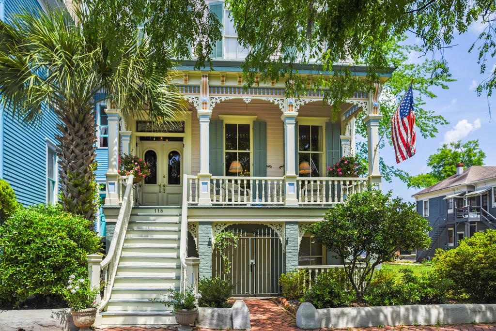 A blue, yellow and white Victorian Home with a porch and a large tree.