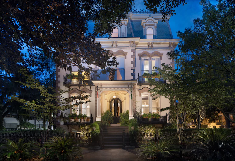 A mansion house lite up in the dark in a tree lined street