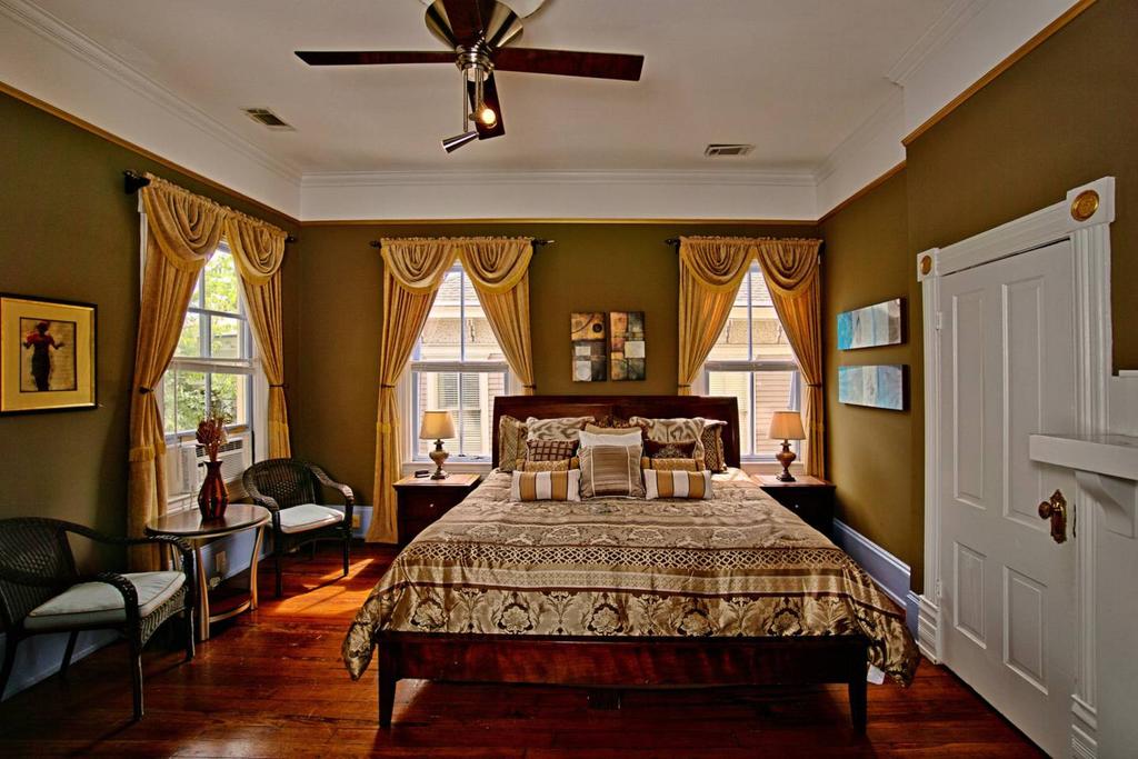 An olive green bedroom and a large wooden bed and green drapes over three widows.