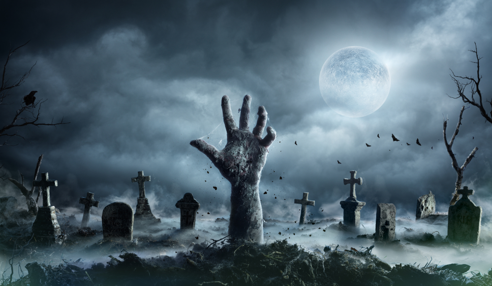A creepy image of a hand sticking out of a grave at night with a full moon