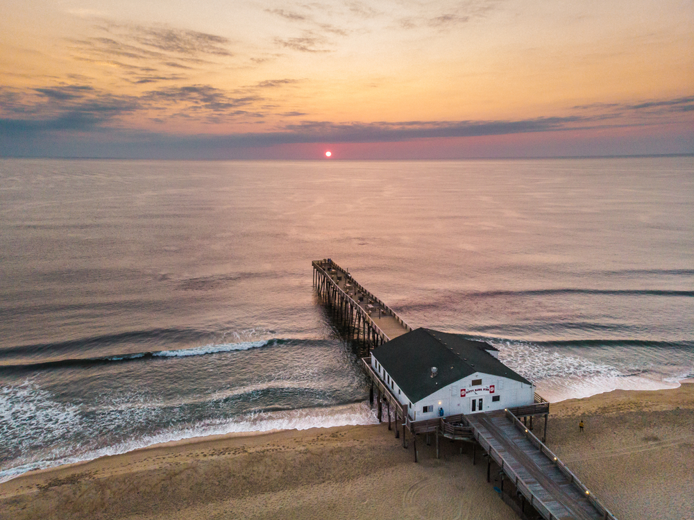 Aerial view of the pier in Kitty Hawk during a pink sunset over the ocean.