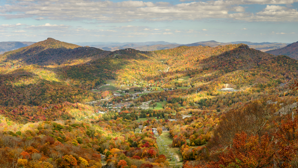 A picture of hills and mountains covered in a sea of trees turning orange and yellow in the fall in Banner Elk.