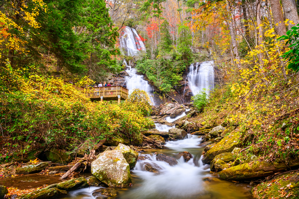 Photo of visitors standing on an observation deck to enjoy the tiered Anna Ruby Falls and surrounding colors of Fall in Georgia. 