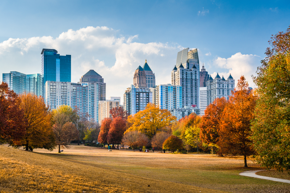 Photo in a field in Piedmont Park where the skyline of Atlanta, Georgia can be seen above a colorful hedge of various trees during Fall in Georgia. 