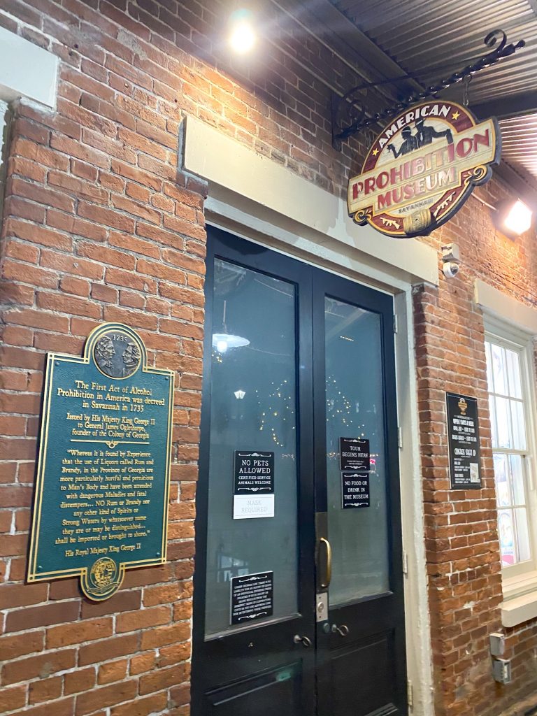 The entrance to the Prohibition Museum in the City Market. It has a brick façade, two double black doors, and a few signs around it explaining its history and hours. A cool place to see during your 3 days in Savannah
