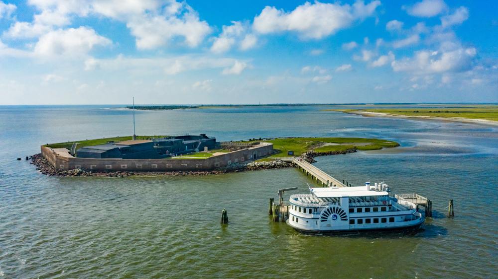 An aerial view of Fort Sumter in South Carolina with a ferry parked outside of it. It is a sunny day with clouds in the sky.