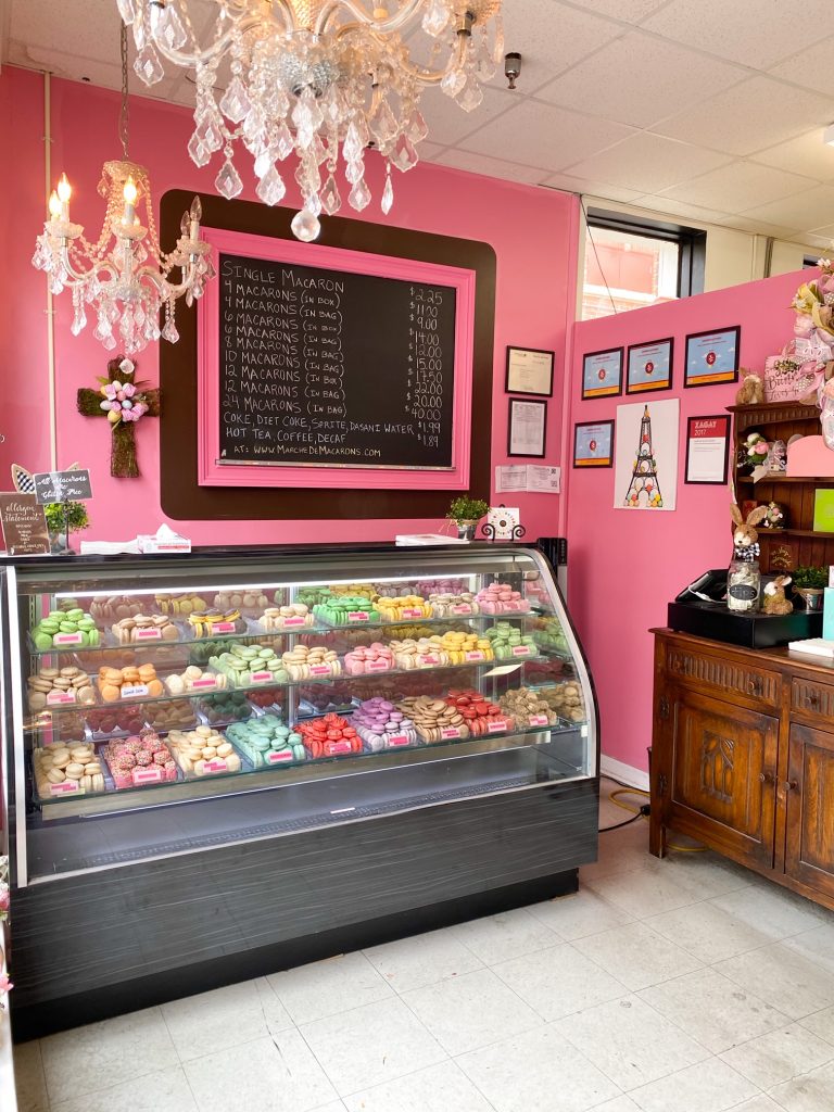 The interior of the Marche de Macarons shop in Savannah. The walls are painted bright pink and there is a large chalkboard with a pink and black frame that lists the menu for the macarons. There is a large refrigerated display case full of macarons of literally every color. A fun place to get dessert during your 3 days in Savannah