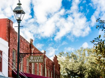 A old sign saying city market on a lamppost with building in the background. City Market is a great place for shopping in Savannah
