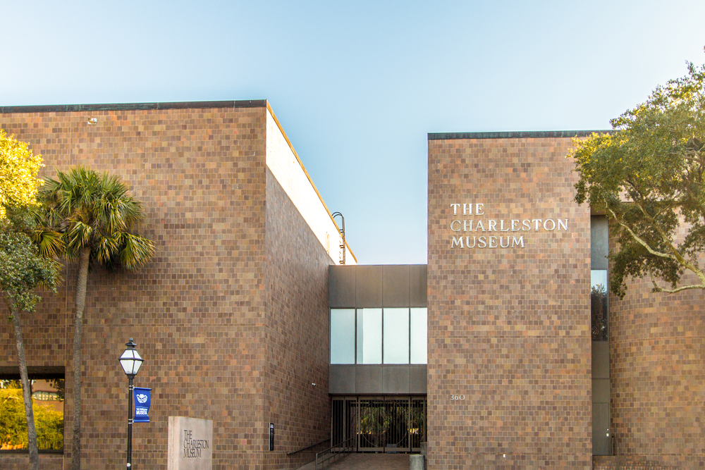 The Charleston Museum entrance, which is a brick building with palm trees outside. The museum's logo is written in silver letters