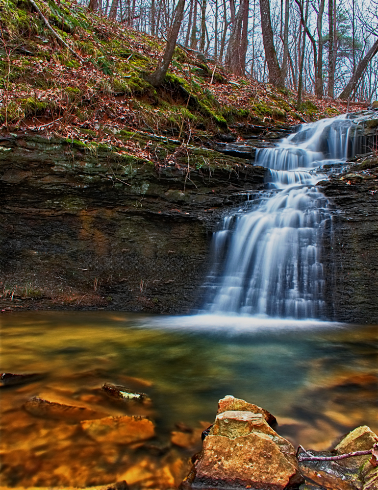 A tiered waterfall cascades down the rocky front into a calm pool. 