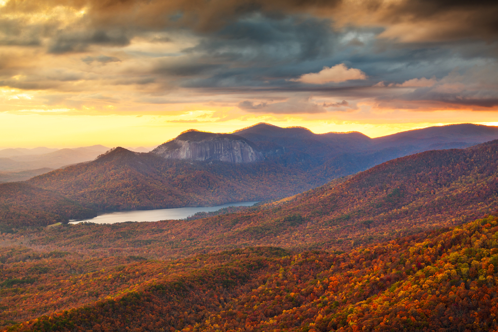 Photo of a foliage-covered mountain landscape with a lake in the distance as seen from the Caesar's Head Overlook, one of the best places to experience fall in South Carolina!