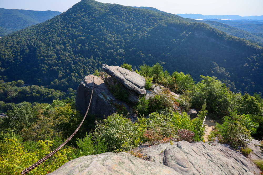 Photo of a large rock with a chain connected to it overlooking a tree-covered mountain landscape at Pine Mountain State Park.