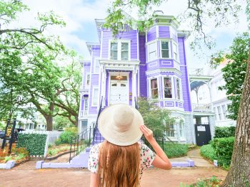 woman holding her hat in front of purple house in Savannah georiga