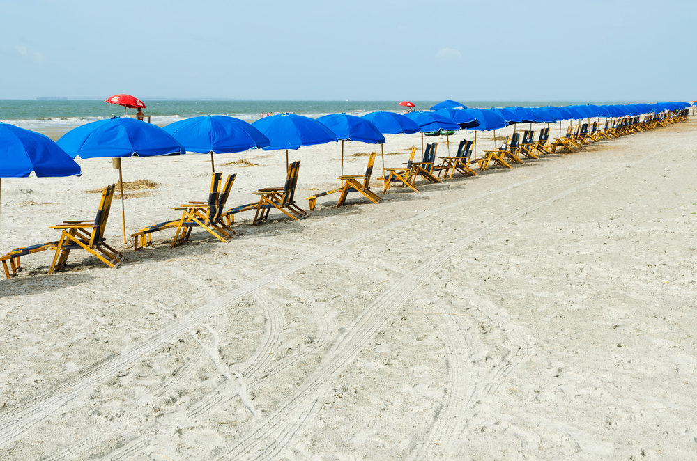 beach chairs lined up along the sand with blue umbrellas 