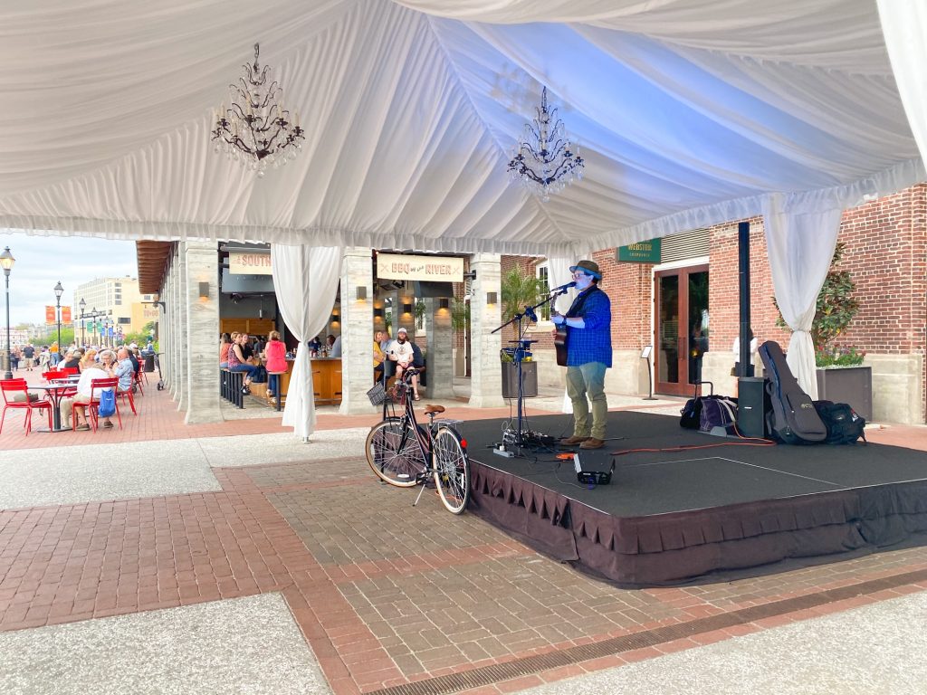 A live musician plays guitar under a covered tarp at the Plant Riverside District. 