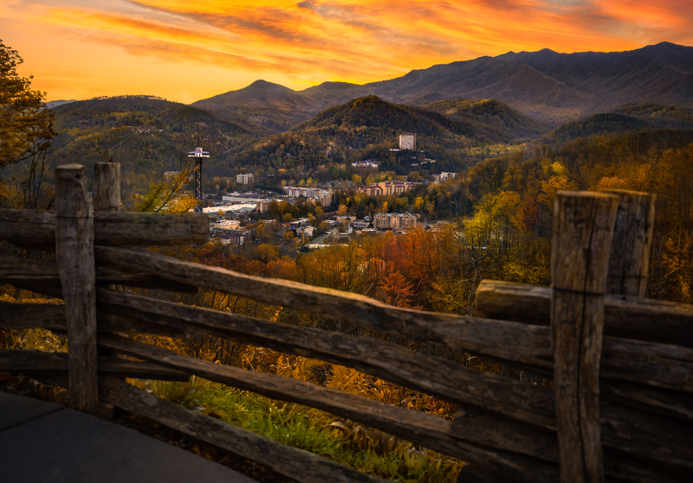 Sunset view from behind a wooden fence looking down at Gatlinburg city in the valley and Mountains in the background taken during fall