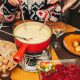 a red pot of cheese fondue in center of table with family dipping in food
