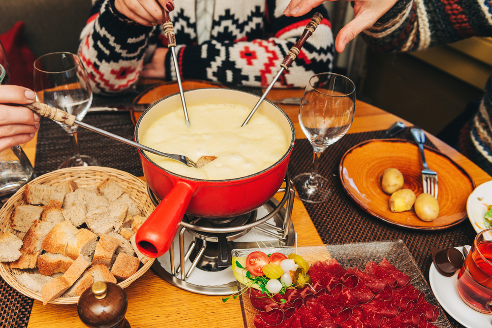 a red pot of cheese fondue in center of table with family dipping in food