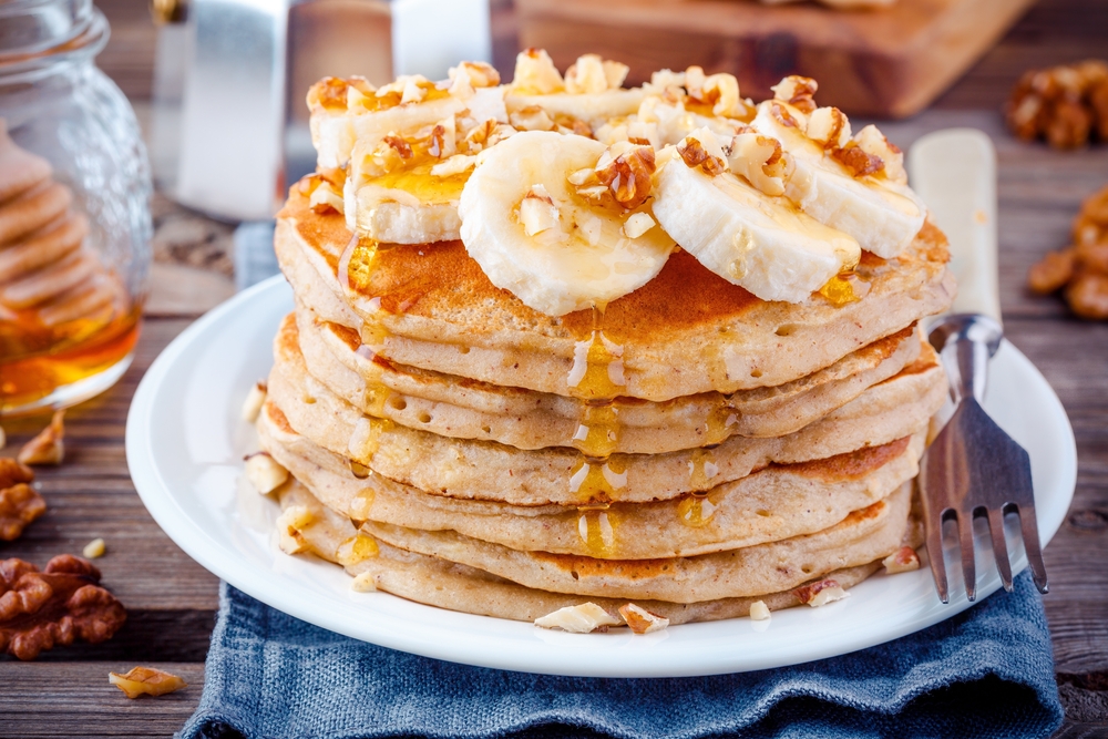 A stack of fluffy pancakes topped with bananas and walnuts and topped with syrup