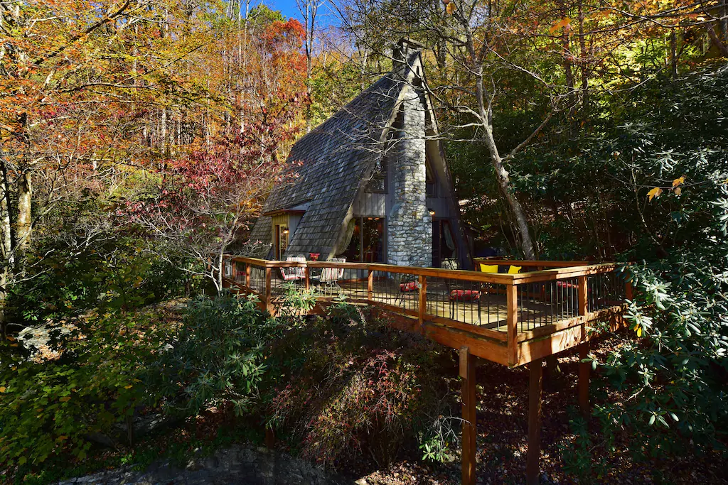 Photo of Chalet Alpine, one of the best Blue Ridge Mountains Cabins, an A-frame cabin with a wood and stone exterior with a large wood deck hanging over a hill.