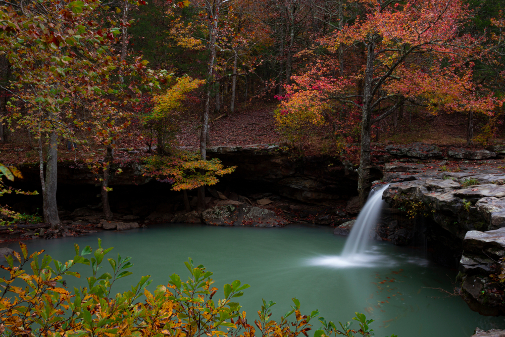 A photo of Falling Water Waterfall pouring into it's pool of blue water with the the trees decorated in fall foliage. 