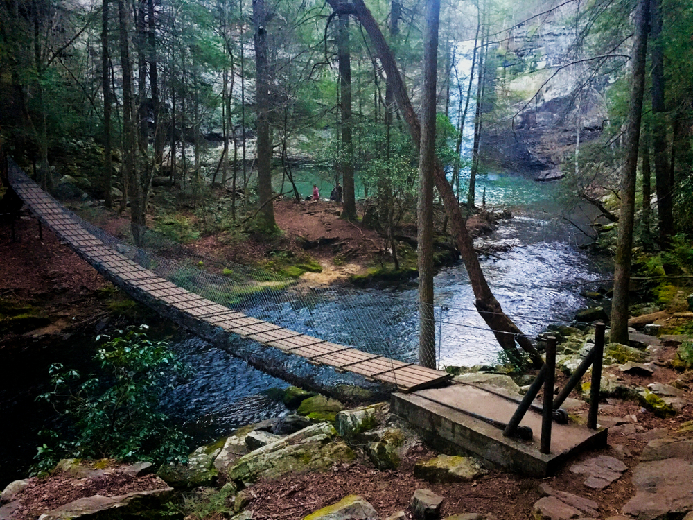 A picture of a suspension bridge and river flowing from the Foster Falls waterfall in South Cumberland State Park in Tennessee.