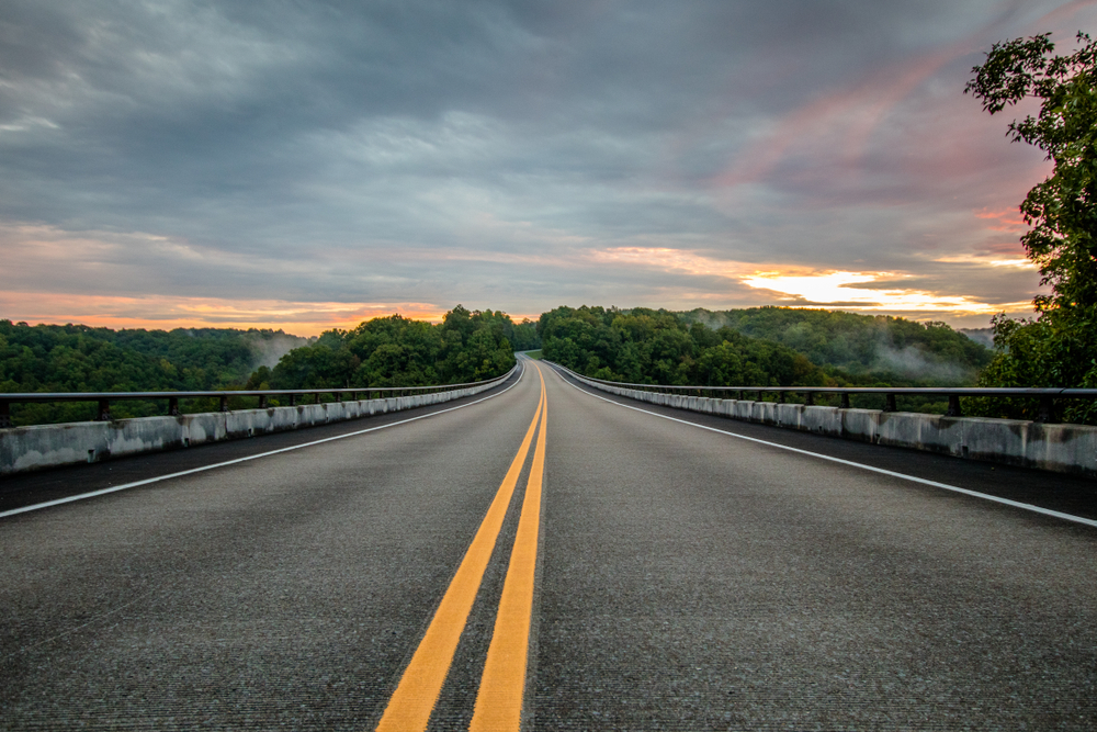 A picture of a long road above a forested area at sunrise along the Natchez Trace Parkway in Tennessee.