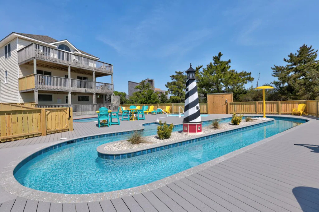 Photo of the backyard of Rio Rodanthe with a lazy river, swimming pool, small kiddie pool, lighthouse statue, and brightly colored patio furniture, 