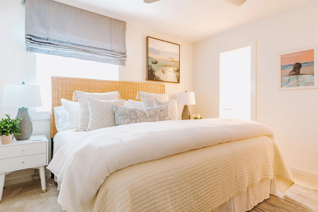 Photo of a bedroom featuring a king-size bed, wicker headboard, and beach artwork in The Treehouse OBX, one the prettiest Outer Banks vacation rentals.