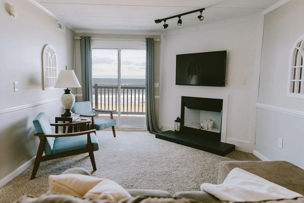 Photo of the living room inside Paradise Plus featuring a balcony overlooking the ocean, tile fireplace, and modern accent chairs one of the best vacation rentals in the outer banks