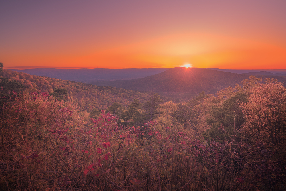 A photo of an orange sunset over the rolling Ozark Mountains in the fall.