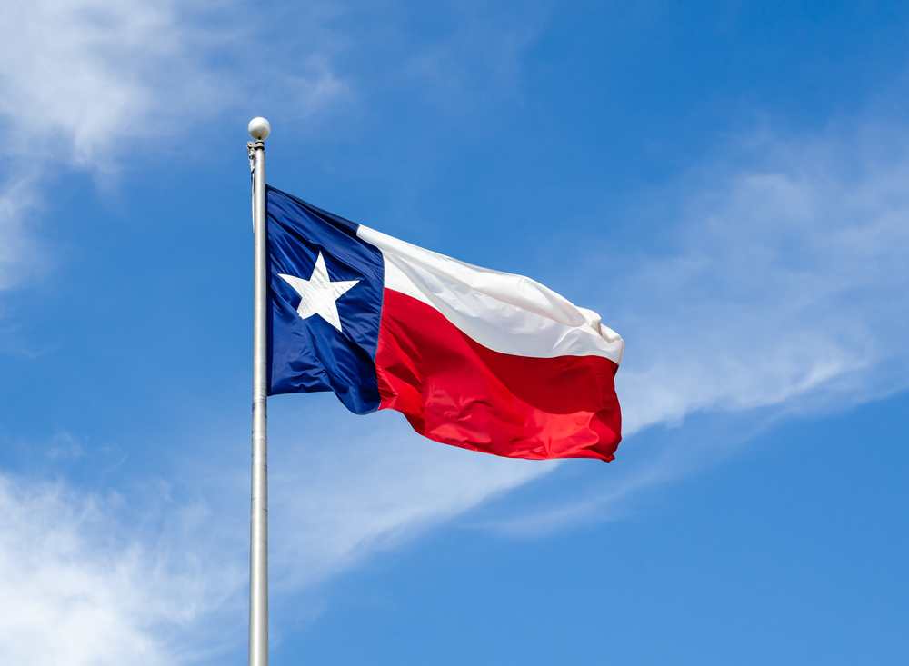 The Texas flag waves on a flag pole on a windy day.